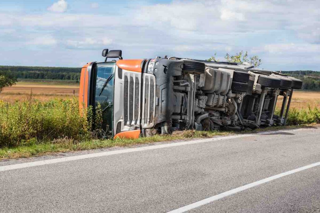 Overturned truck in a field next to road