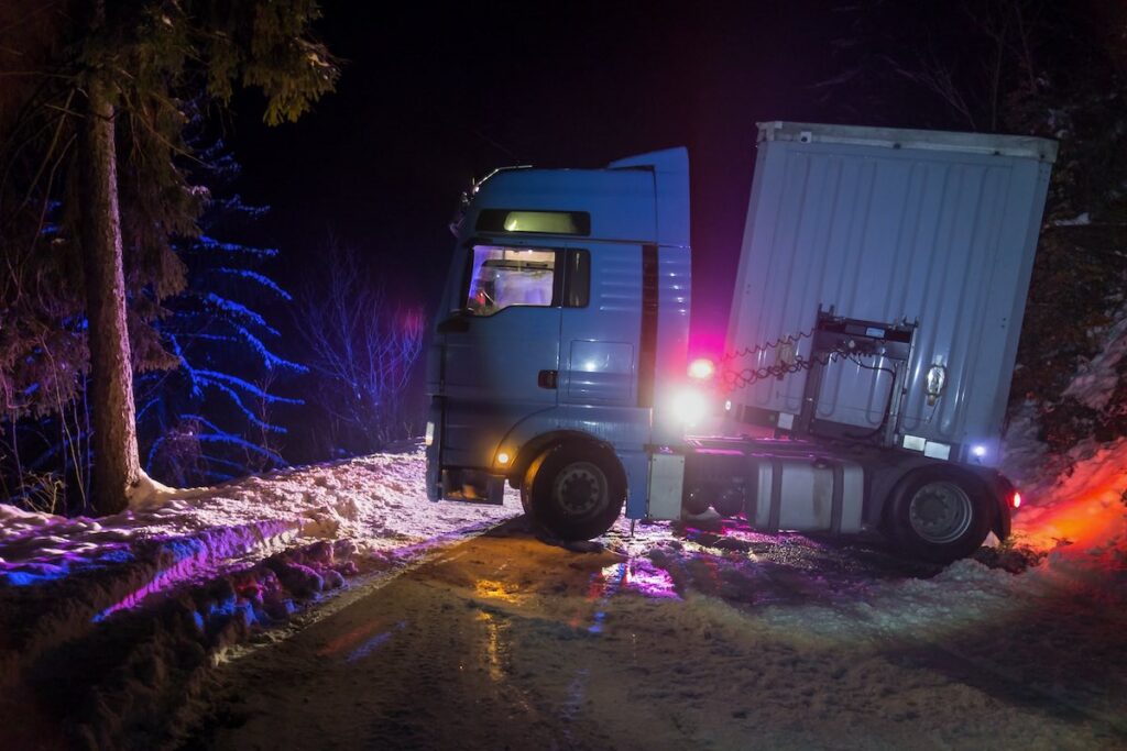 Jackkife semi truck traffic accident at night, on a snowy winter road. Broken truck on the road in the snow.