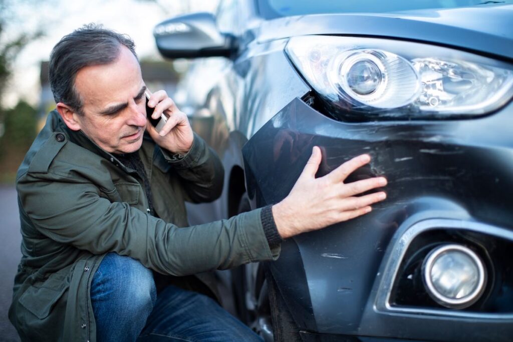 Unhappy male driver looking at the damaged car after a road accident