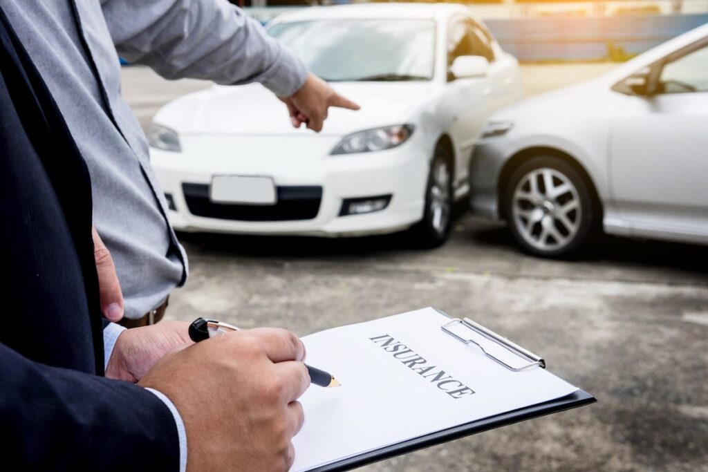 Insurance agent writing on clipboard while examining car after accident claim being assessed and processed