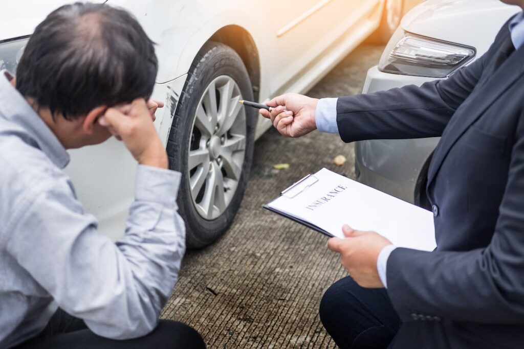 Farmers insurance agent writing on clipboard while examining car after an accident