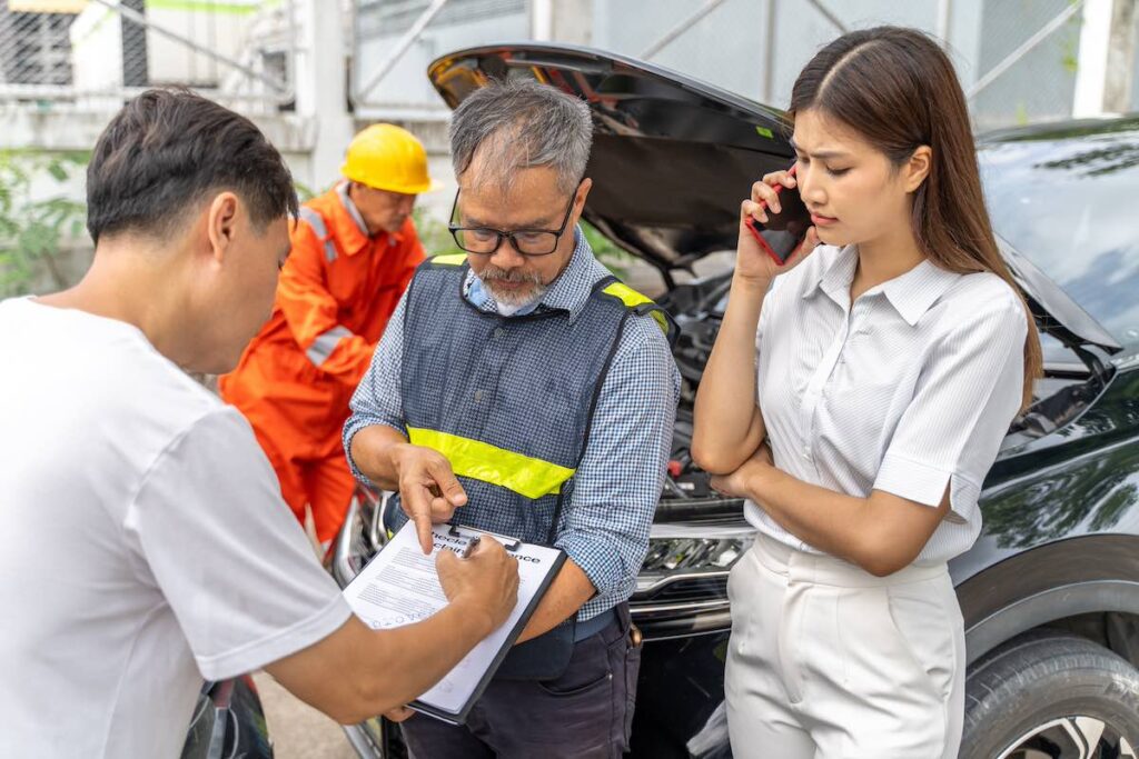 A Kemper insurance agent showing the male customer where to sign the car insurance claim form while female car owner standing beside them talking on her phone