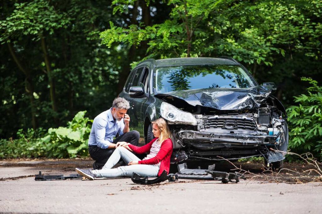 Young shocked woman by the car after an accident and a man making a phone call