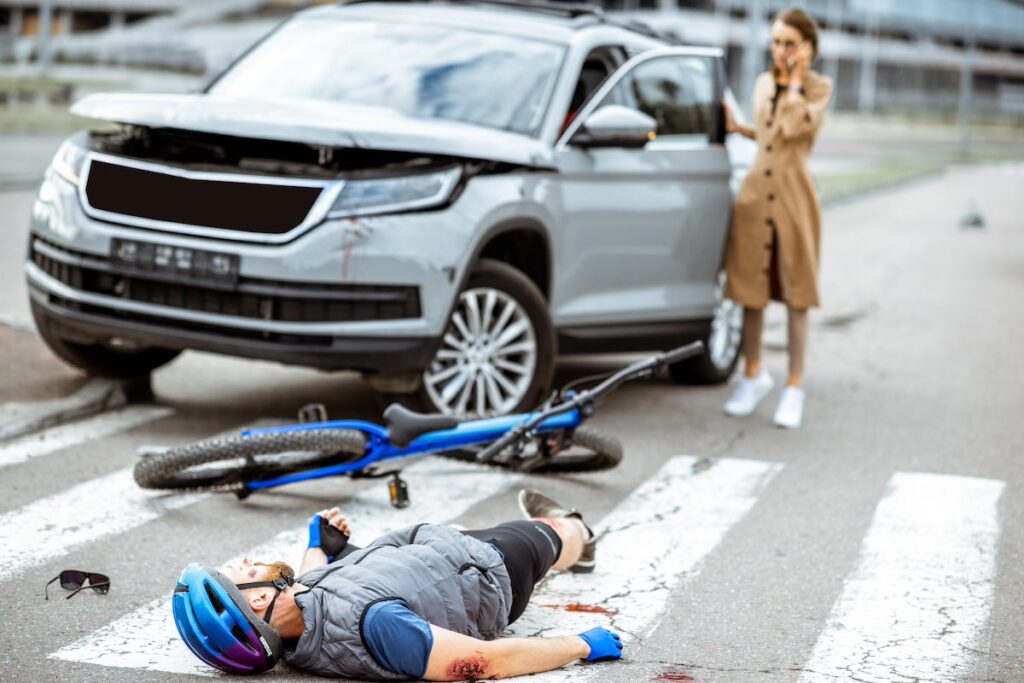 Road accident in Oregon with injured cyclist lying on the pedestrian crossing and a worried woman driver